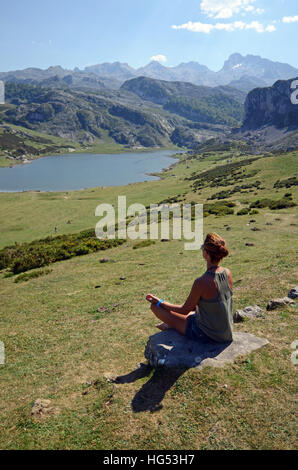 Junge Frau sitzt in Lotus Pose vor einem der Covadonga Seen, Asturien Stockfoto