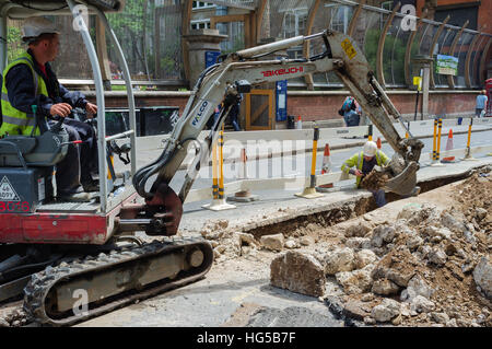 Ein Mann, der einen Bagger betreibt, während ein anderer Mann im Graben in der Wardour Street in der Stadt London, England, Großbritannien, steht. Stockfoto