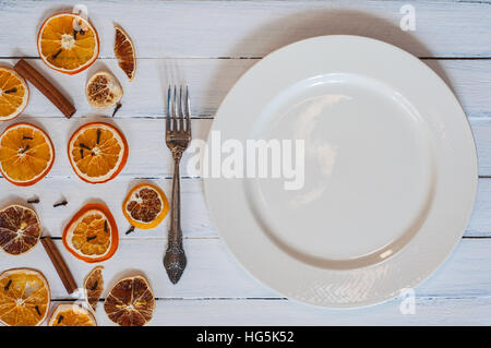 Weißen leeren Teller mit einer Gabel auf eine weiße Vintage Holzoberfläche, serviert mit trockenen Scheiben von Zitrusfrüchten, Ansicht von oben Stockfoto