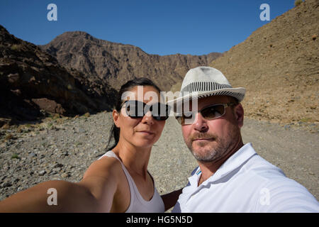Ein Paar mittleren Alters macht ein fröhliches Selfie in einem wunderschönen Wadi, einem trockenen Flussbett im Nahen Osten, und zeigt ihr Reiseerlebnis Stockfoto