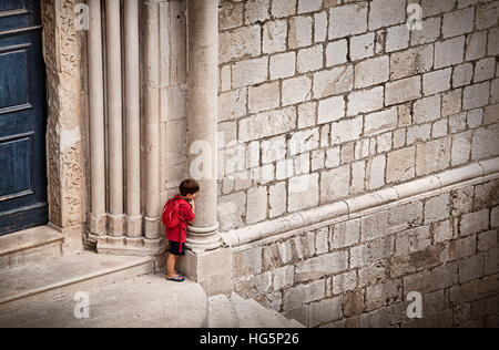 Kleiner Junge versteckt sich hinter der Säule rot Stockfoto