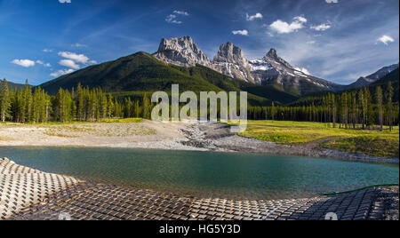 Three Sisters Mountain Peak, Panoramalandschaft im Grünen Wald mit blauer Skyline und Reservoir im Vordergrund. Canmore, Alberta, Kanadische Rockies Stockfoto