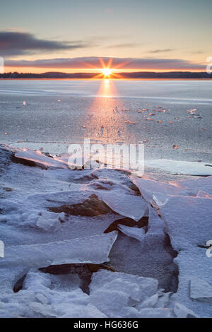 Sunrise und Gestein unter gestoßenem Eis auf einem gefrorenen See in Finnland im Winter. Stockfoto