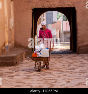 Ksar Elkhorbat, Marokko.  Junge Frau bringt Wasser in ihre Schubkarre in der Kasbah. Stockfoto