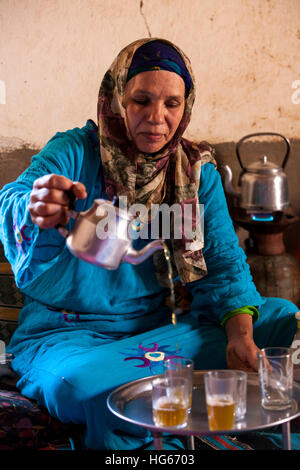 Ksar Elkhorbat, Marokko.  Mittleren Alters Amazigh Berber Frau Gießen Tee in ihrem Wohnzimmer. Stockfoto