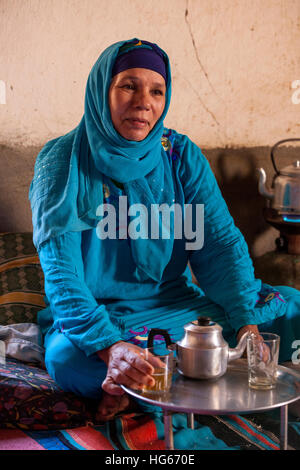 Ksar Elkhorbat, Marokko.  Mittleren Alters Amazigh Berber Frau trinken Tee in ihrem Wohnzimmer. Stockfoto