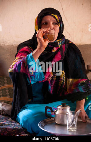 Ksar Elkhorbat, Marokko.  Mittleren Alters Amazigh Berber Frau trinken Tee in ihrem Wohnzimmer. Stockfoto