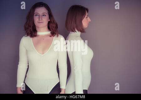 Doppelgänger / Alter Ego unter dem Motto Fotoshooting: zwei junge Frauen Mädchen tragen passende Kleidung Stand zusammenstehen passende Echo Spiegelung jedes andere körperliche Haltung und Ausdruck - Stand zurück um zu zurück blicken nicht auf einander Stockfoto