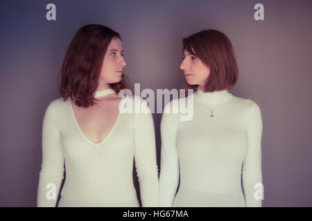 Doppelgänger / Alter Ego unter dem Motto Fotoshooting: zwei junge Frauen Mädchen passende Kleidung Stand stehend zusammen passende Echo Spiegelung jedes andere körperliche Haltung und Ausdruck - stehen nebeneinander, einander betrachtend Stockfoto