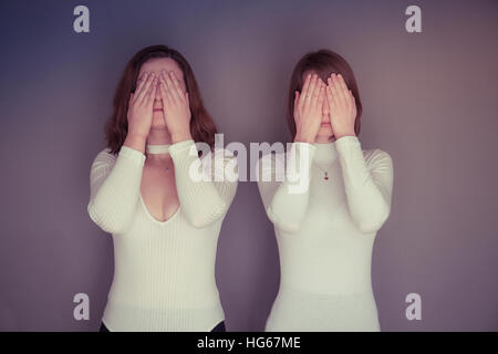 Doppelgänger / Alter Ego unter dem Motto Fotoshooting: zwei junge Frauen Mädchen tragen passende Kleidung Stand zusammen stehen passende Echo Spiegelung jedes andere körperliche Haltung und Ausdruck - zwei Hände für ihre Augen - sehen, nichts Böses Stockfoto