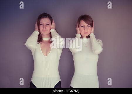 Doppelgänger / Alter Ego unter dem Motto Fotoshooting: zwei junge Frauen Mädchen tragen passende Kleidung Stand zusammen stehen passende Echo Spiegelung jedes andere physische darstellen und Ausdruck - Hände über die Ohren – hören, nichts Böses Stockfoto