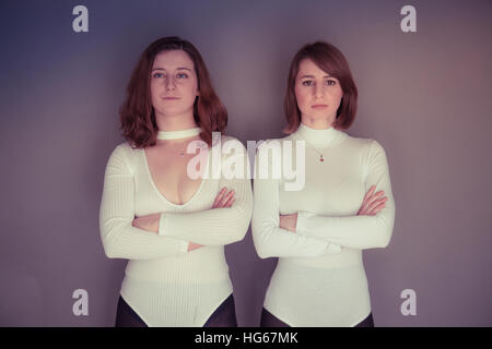 Doppelgänger / Alter Ego unter dem Motto Fotoshooting: zwei junge Frauen Mädchen tragen passende Kleidung Stand zusammen stehen passende Echo Spiegelung jedes andere physische darstellen und Ausdruck - Arme gefaltet Stockfoto