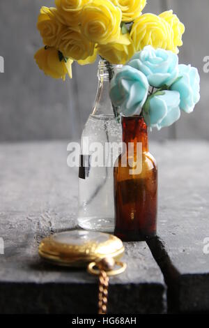 Blumen in Flaschen auf Vintage Holztisch und goldene Taschenuhr. Stockfoto