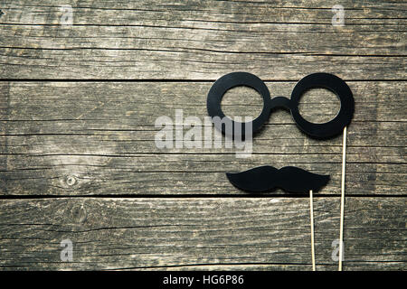 Fake Brille und Schnurrbärte auf Stöcken auf alten hölzernen Hintergrund. Stockfoto