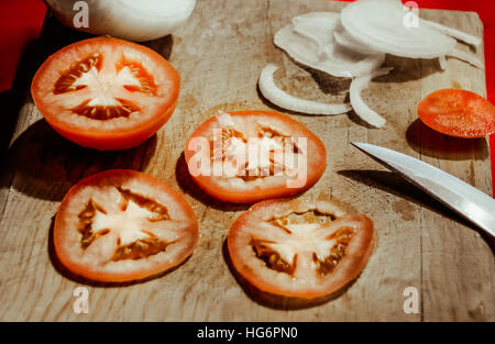 Foto von einem Messer, Tomatenscheiben und Zwiebeln auf ein Holz Schneidebrett Stockfoto