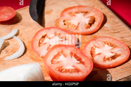 Foto von einem Messer, Tomatenscheiben und Zwiebeln auf ein Holz Schneidebrett Stockfoto