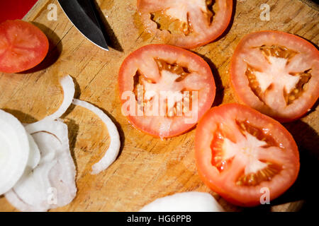 Foto von einem Messer, Tomatenscheiben und Zwiebeln auf ein Holz Schneidebrett Stockfoto