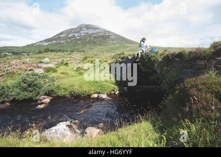 Einsamer Wanderer Stand auf einer alten Brücke in der vergifteten Glen mit Blick auf Mount Errigal. Glenveagh Nationalpark, County Donegal, ich Stockfoto