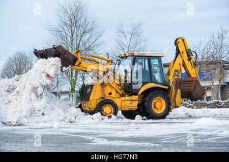 Baggerlader Schneeräumung von einem Parkplatz auf einen Haufen. Stockfoto