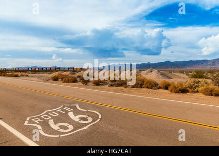 USA Route 66 Autobahn mit Zeichen auf Asphalt und ein langer Zug im Hintergrund, in der Nähe von amboy, Kalifornien. Das Hotel liegt in der Mojave-Wüste Stockfoto