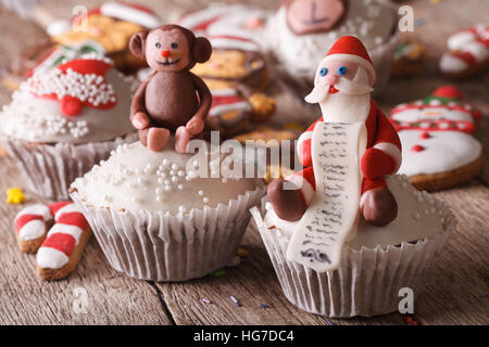 Weihnachts-Muffins mit Figuren des Santa und Affen hautnah auf einem Holztisch geschmückt. horizontale Stockfoto