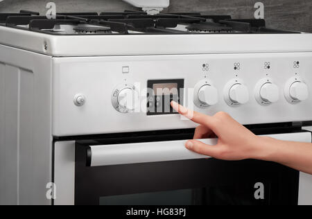 Weibliche Hand drehen auf weiße Küche Gasherd auf grauem Hintergrund Stockfoto