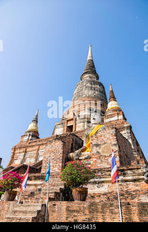 Buddha-Statue am unteren Rand eine große alte Pagode auf blauen Himmelshintergrund am Wat Yai Chai Mongkon Tempel in Phra Nakhon Si Ayutthaya Historical Stockfoto