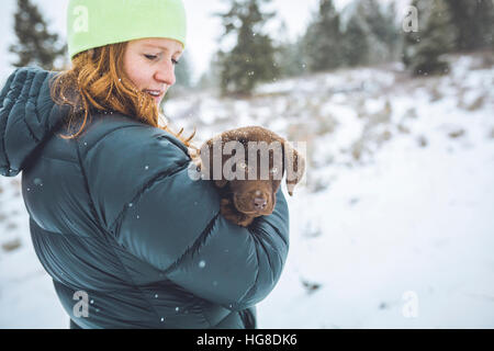 Seitenansicht der Frau mit Chocolate Labrador stehend auf schneebedecktes Feld Stockfoto