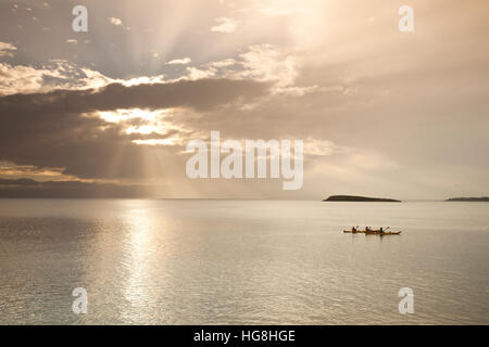 DREI Kajakfahrer auf ruhiger See Kajak mit Sonne hinter Wolken mit Gottes Sonnenstrahlen in Wineglass Bay, Tasmanien Stockfoto