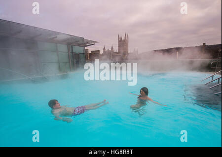 Dampf steigt oberhalb der heißen natürlichen Quellwasser auf der Dachterrasse Spa Thermae Bath Spa, wie Leute den Blick genießen auf Bath Abbey kontrastierenden heißes Wasser und Temperaturen unter dem Gefrierpunkt draußen während der Kältewelle in Teilen des Vereinigten Königreichs. Stockfoto