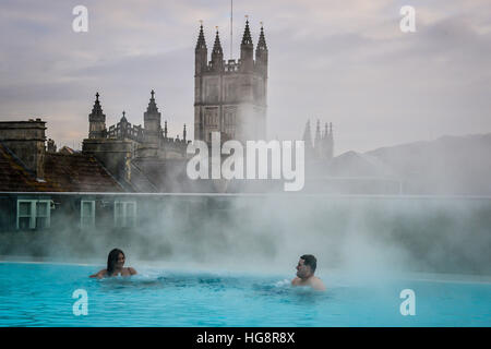 Dampf steigt oberhalb der heißen natürlichen Quellwasser auf der Dachterrasse Spa Thermae Bath Spa, wie Leute den Blick genießen auf Bath Abbey kontrastierenden heißes Wasser und Temperaturen unter dem Gefrierpunkt draußen während der Kältewelle in Teilen des Vereinigten Königreichs. Stockfoto