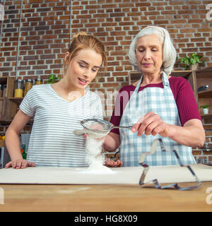 Großmutter und Enkelin Sichtung Mehl für Cookies in Küche Stockfoto
