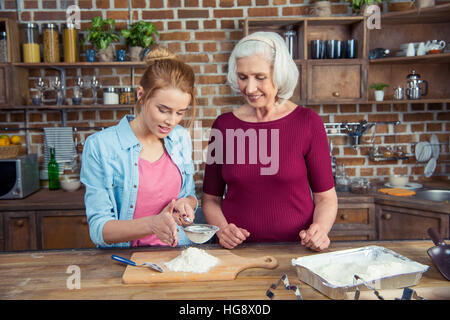 Großmutter und Enkelin Sichtung Mehl für Cookies in Küche Stockfoto