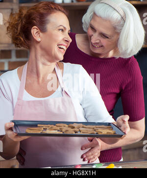 Mutter und Erwachsene Tochter hält Backblech mit Weihnachtsgebäck Stockfoto