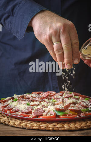 Mann in ein blaues Hemd mit Käse Pizza auf den Tisch vertikale bestreuen Stockfoto