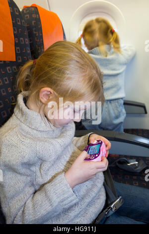 Kind zwei Kinder im Alter von 6 & 2 gehen im Urlaub / Urlaub spielen Videospiel & Blick aus Fenster auf Luft Flugzeug fliegen / Flugzeug Flug Stockfoto