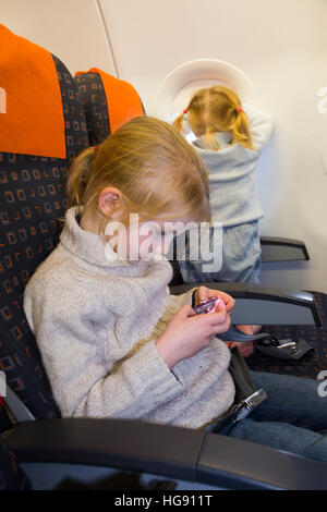 Kind zwei Kinder im Alter von 6 & 2 gehen im Urlaub / Urlaub spielen Videospiel & Blick aus Fenster auf Luft Flugzeug fliegen / Flugzeug Flug Stockfoto