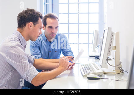 Zwei glückliche Kollegen diskutieren gemeinsam über ein Projekt oder eine Zusammenarbeit in helle moderne Büroeinrichtung mit Computern Stockfoto