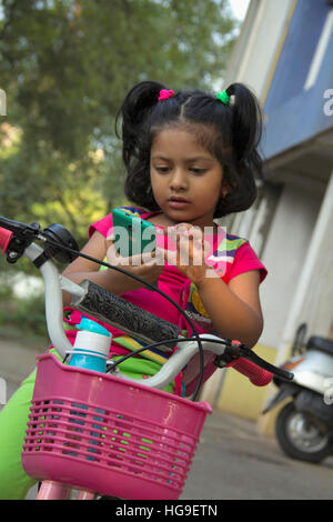 Kleine Inderin beim Sitzen auf dem Fahrrad mobile Kontrolle Stockfoto