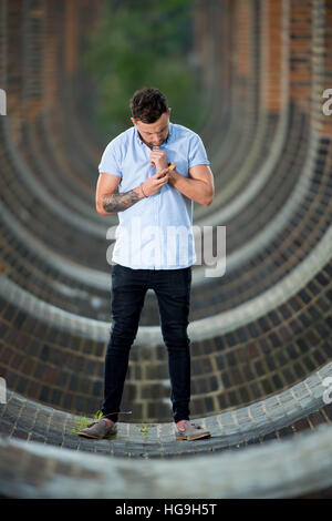 Sänger, posiert Songwriter Jamie Mathias mit seiner Gitarre für ein Shooting an der Ouse Valley-Viadukt, Sussex, UK. Stockfoto