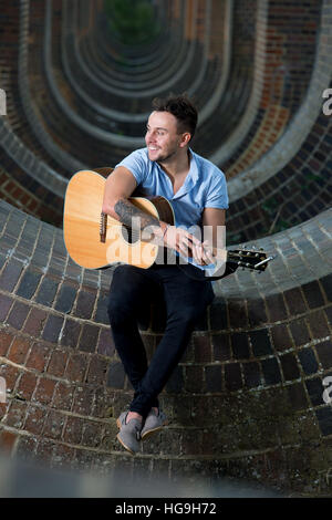 Sänger, posiert Songwriter Jamie Mathias mit seiner Gitarre für ein Shooting an der Ouse Valley-Viadukt, Sussex, UK. Stockfoto