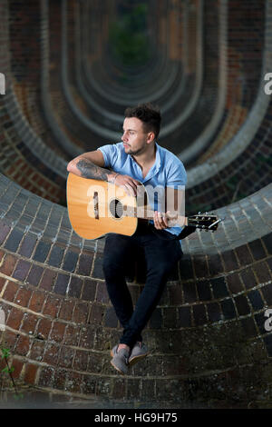 Sänger, posiert Songwriter Jamie Mathias mit seiner Gitarre für ein Shooting an der Ouse Valley-Viadukt, Sussex, UK. Stockfoto