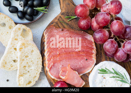 Wurstwaren, frisches Baguette, Trauben, Käse und schwarzen Oliven. Italienische Antipasti festgelegt. Nahaufnahme Stockfoto