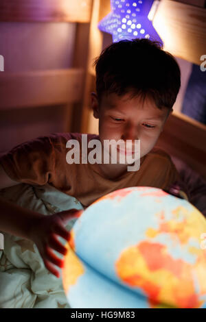 Kleiner Junge Länder auf der ganzen Welt zu entdecken, in der Nacht im Bett studieren Stockfoto