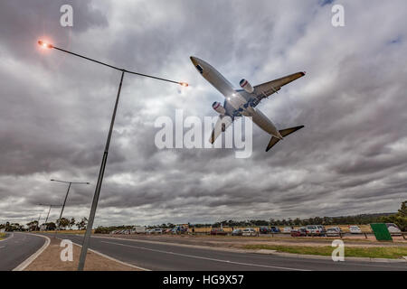 Passagierjet Flugzeug fliegen niedrig am Himmel direkt über leuchtenden Straßenlaternen bei stürmischem Wetter Stockfoto