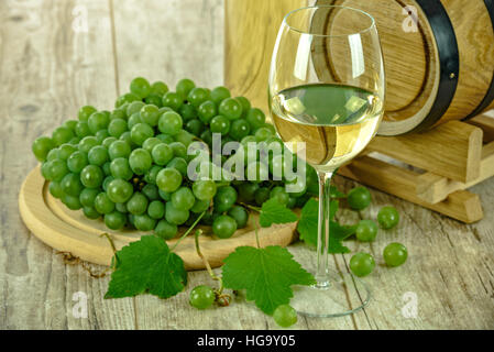 Halb süßen Weißwein in der Tasse neben frischen Trauben und einem Holzfass Stockfoto