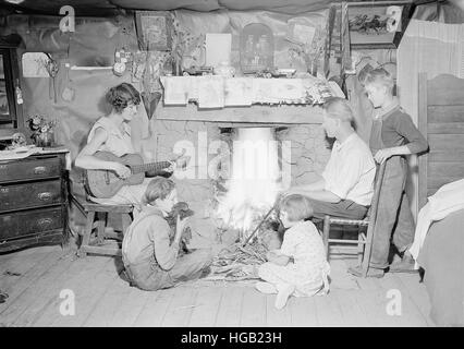 Mutter spielt Gitarre, während Familie rund um den Kamin 1933 versammelt. Stockfoto