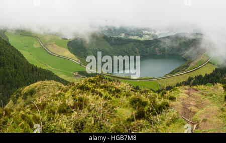 Straße um Lagoa de Santiago. Eine geschwungene Landstraße Schleifen rund um einen See tief in einen steilen alten Vulkankrater. Wolken Eingreifen von oben. Stockfoto