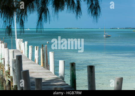 Dock und das Siegel der Abaco. Ein hölzerne Dock führt das Auge zu den ruhigen Gewässern des Meeres.  Segelndes schmuddelig ist off Shore und einem Motorboot festgemacht. Stockfoto