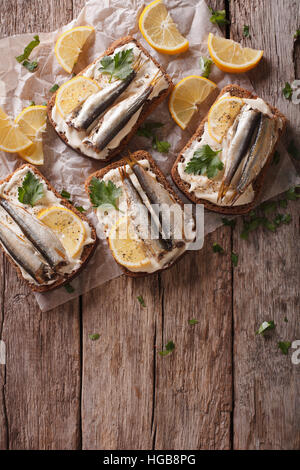 Sandwiches mit Sprotten, Frischkäse und Zitrone auf dem Tisch. vertikale Ansicht von oben Stockfoto